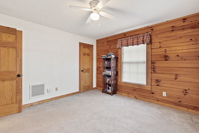 carpeted spare room with ceiling fan and wooden walls