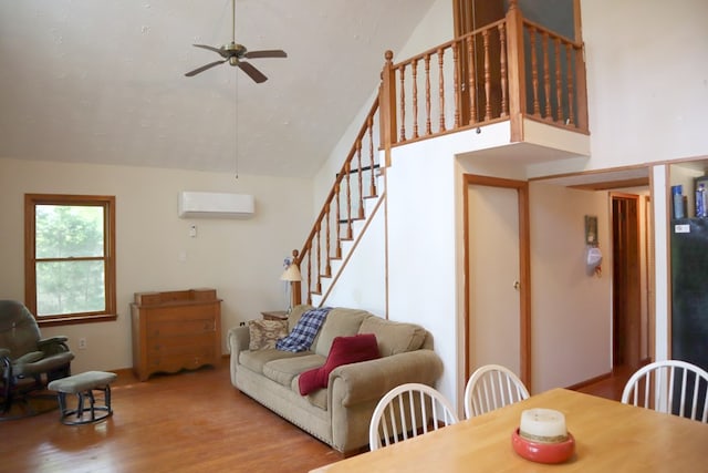 living area featuring an AC wall unit, stairs, wood finished floors, ceiling fan, and vaulted ceiling