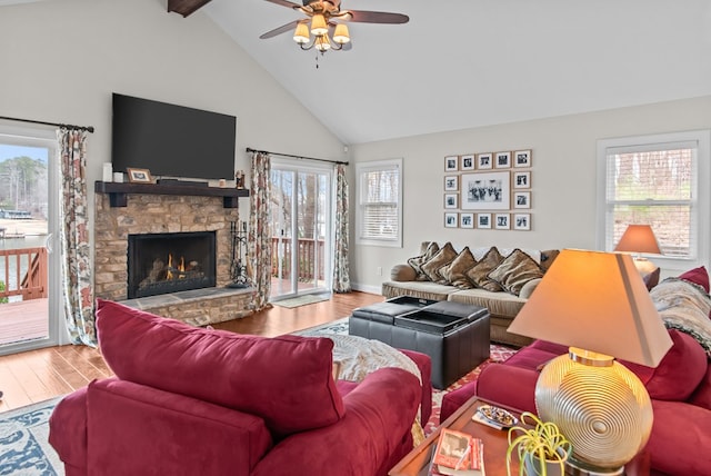 living room with hardwood / wood-style flooring, a stone fireplace, high vaulted ceiling, and beamed ceiling