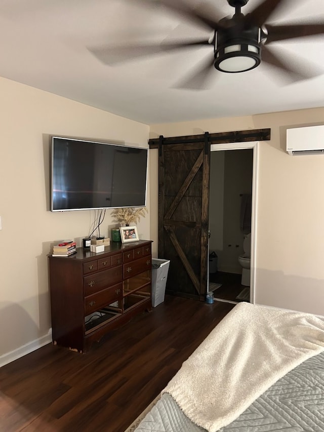 bedroom featuring dark hardwood / wood-style floors, a wall unit AC, ceiling fan, ensuite bathroom, and a barn door