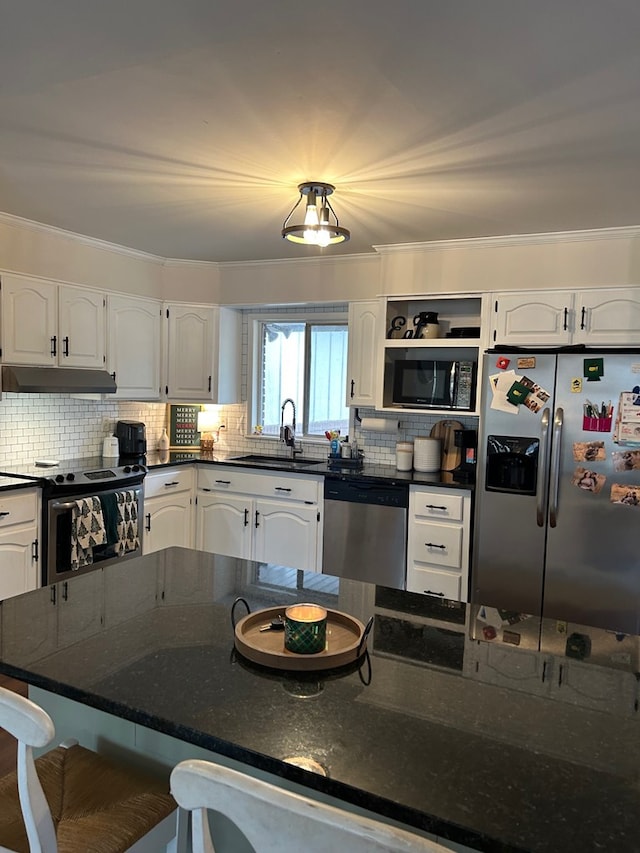 kitchen featuring white cabinets, a kitchen bar, stainless steel appliances, dark stone counters, and sink