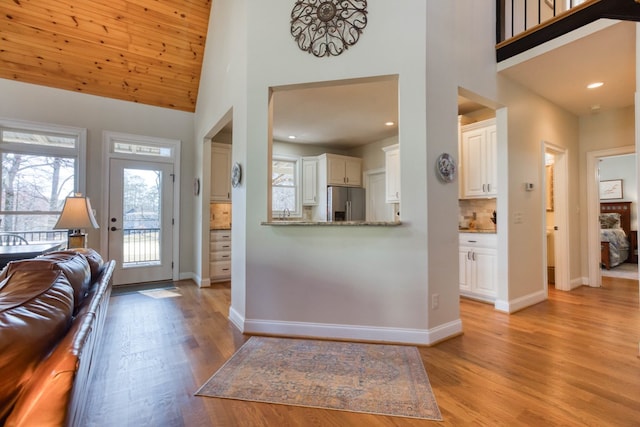 entryway with baseboards, light wood finished floors, and high vaulted ceiling