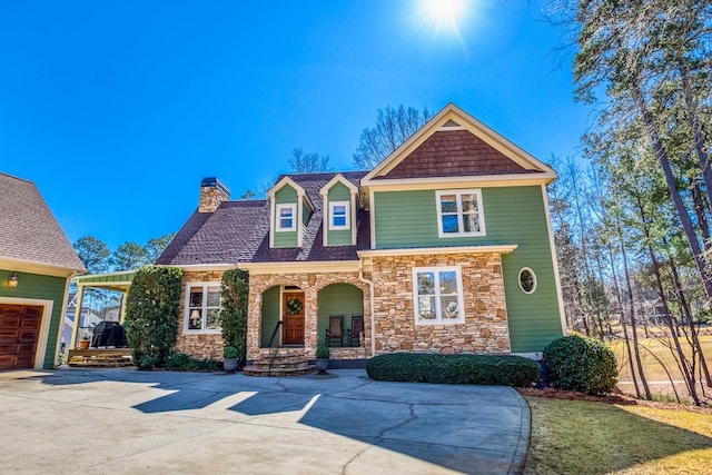 view of front of property with stone siding, covered porch, concrete driveway, a garage, and a chimney