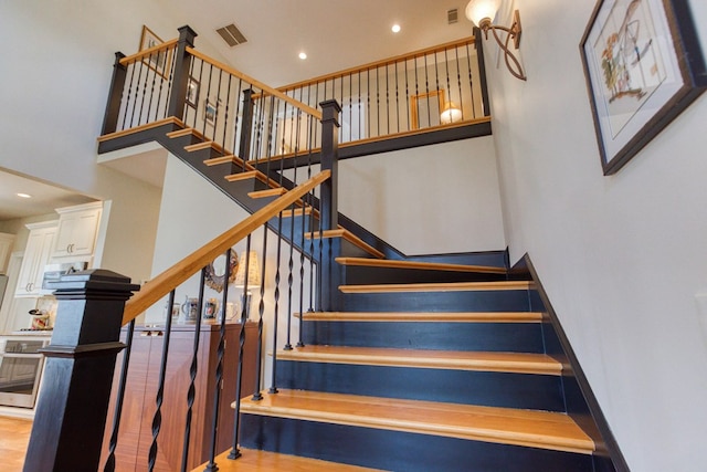 stairway featuring visible vents, baseboards, a towering ceiling, and wood finished floors