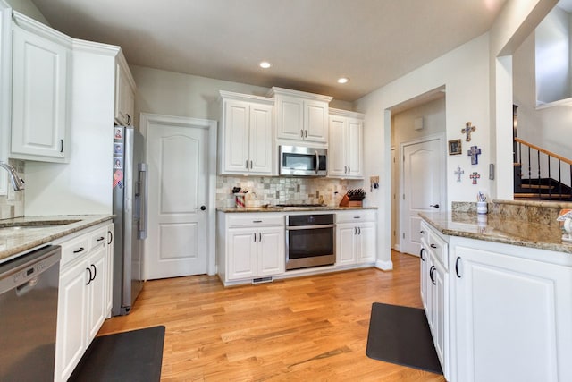 kitchen featuring a sink, white cabinets, light wood-style floors, appliances with stainless steel finishes, and backsplash