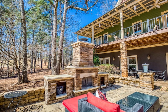 view of patio with an outdoor living space with a fireplace and a balcony