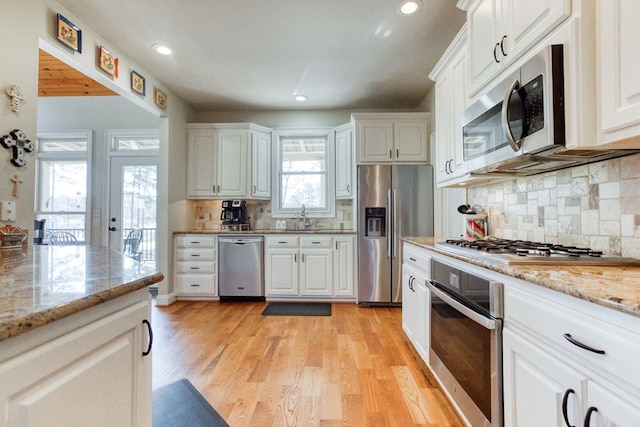 kitchen with white cabinetry, light stone counters, light wood-type flooring, and appliances with stainless steel finishes