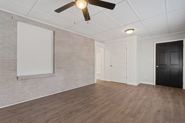 empty room with a paneled ceiling, dark hardwood / wood-style floors, ceiling fan, and brick wall