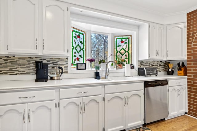 220 Oconnor Dr, Milledgeville, GA 31061 - kitchen featuring stainless steel dishwasher, a sink, white cabinets, decorative backsplash, and brick wall