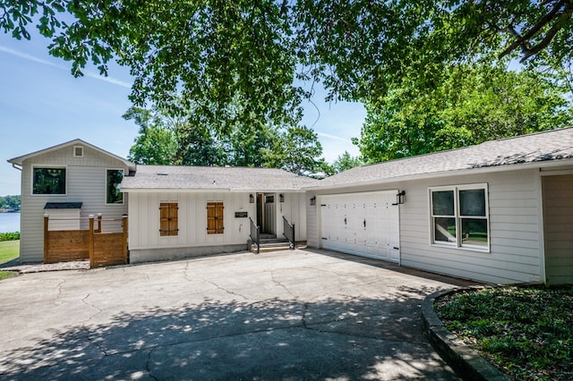 view of front of house with driveway, roof with shingles, an attached garage, fence, and board and batten siding