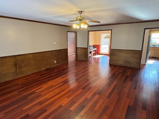 unfurnished room with ornamental molding, ceiling fan, dark wood-type flooring, and wainscoting