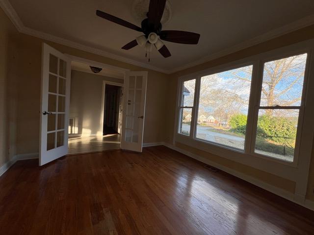 empty room featuring french doors, crown molding, and dark wood-type flooring