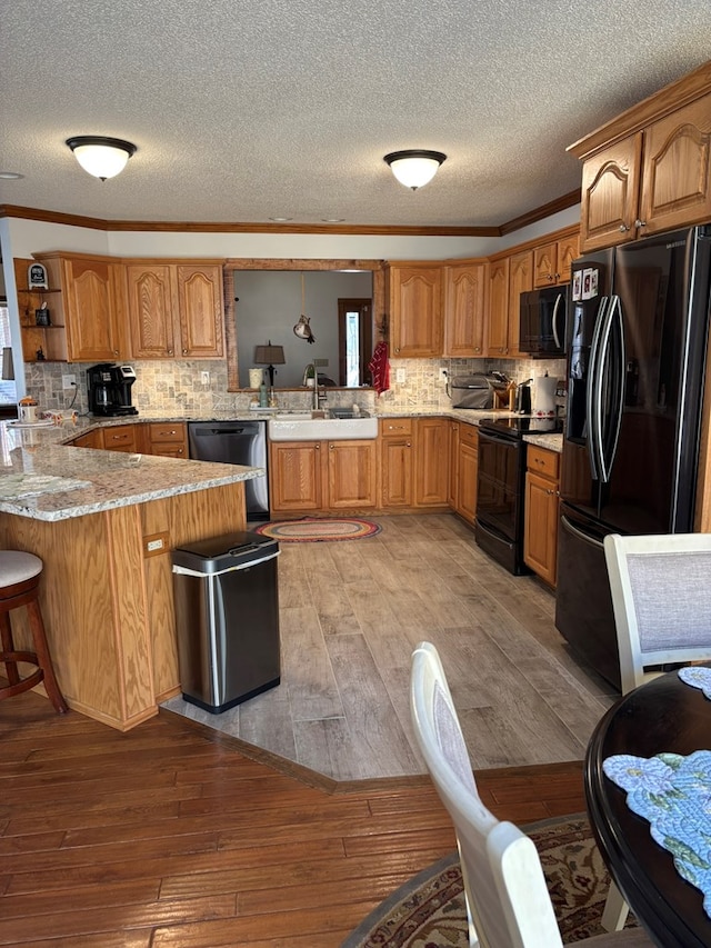 kitchen with light wood-style flooring, brown cabinets, a peninsula, black appliances, and a kitchen bar