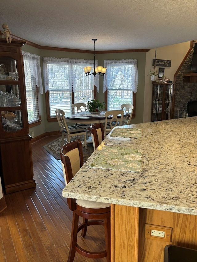 kitchen with a textured ceiling, a notable chandelier, dark wood-type flooring, light stone countertops, and pendant lighting