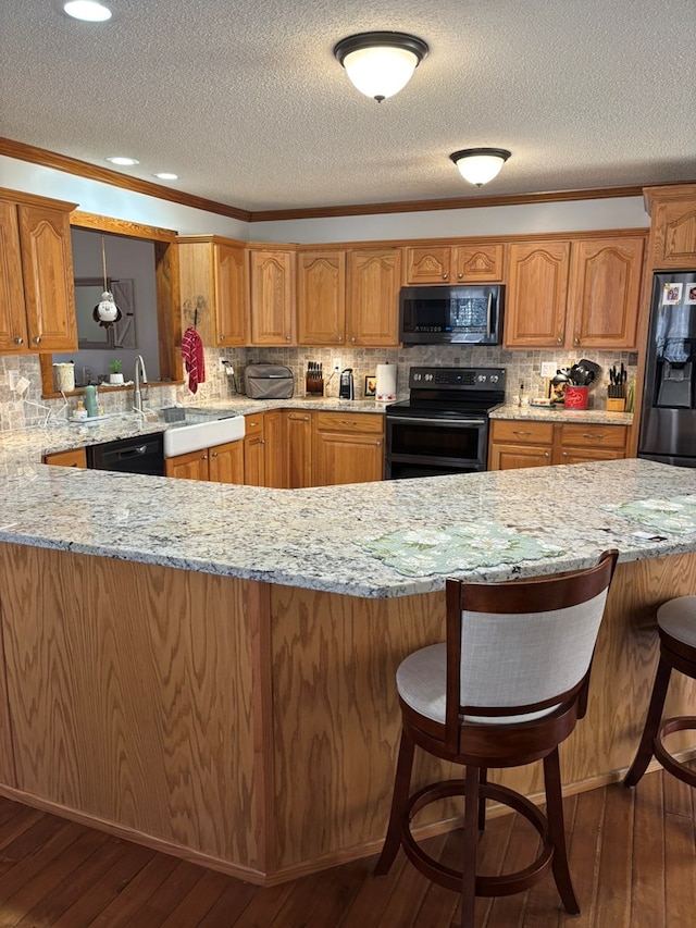 kitchen with brown cabinetry, hanging light fixtures, a peninsula, and black appliances