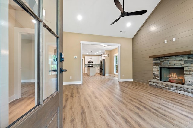 172 Southshore Rd, Eatonton, GA 31024 - unfurnished living room featuring light wood-type flooring, a ceiling fan, a stone fireplace, wooden walls, and high vaulted ceiling