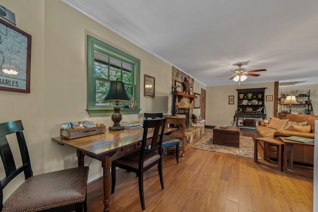 dining space featuring wood finished floors, ornamental molding, a ceiling fan, and a stone fireplace