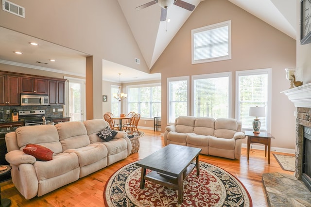 living room featuring ceiling fan with notable chandelier, crown molding, light hardwood / wood-style flooring, a fireplace, and plenty of natural light