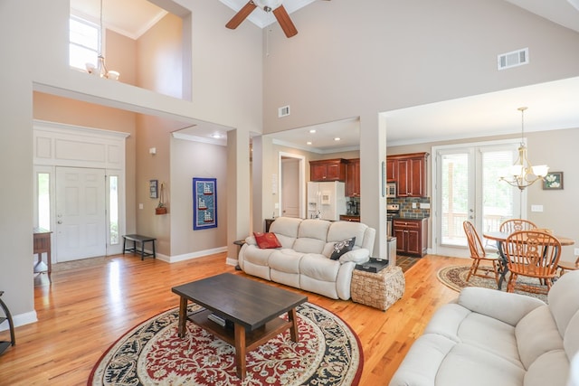 living room featuring crown molding, a towering ceiling, light hardwood / wood-style floors, and ceiling fan with notable chandelier