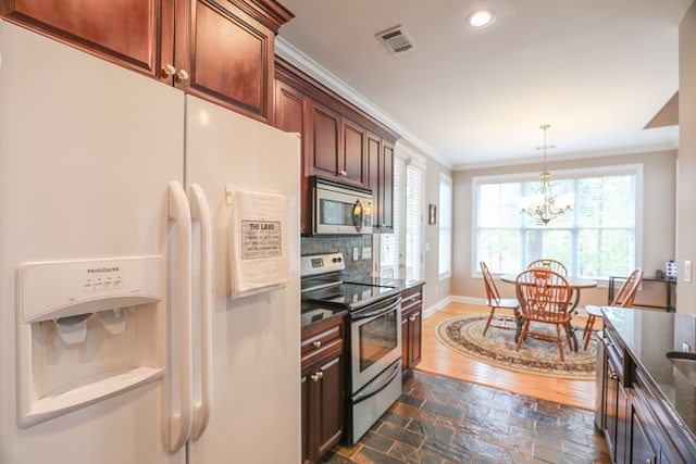 kitchen featuring ornamental molding, dark stone counters, stainless steel appliances, a notable chandelier, and hanging light fixtures