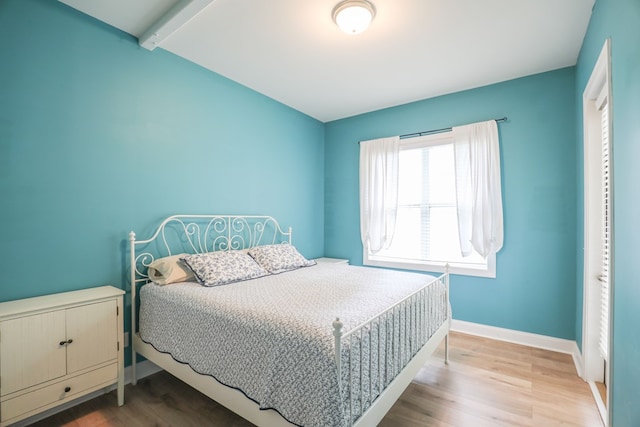 bedroom with beamed ceiling and light hardwood / wood-style floors