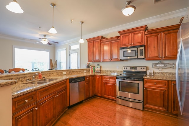 kitchen featuring sink, hanging light fixtures, stainless steel appliances, light stone counters, and ornamental molding