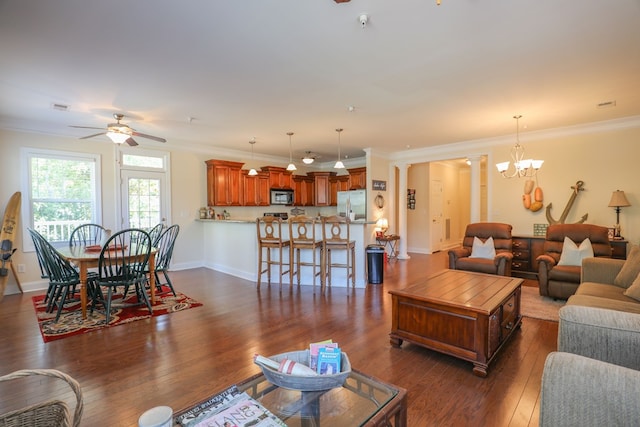 living room featuring ornate columns, crown molding, dark wood-type flooring, and ceiling fan with notable chandelier