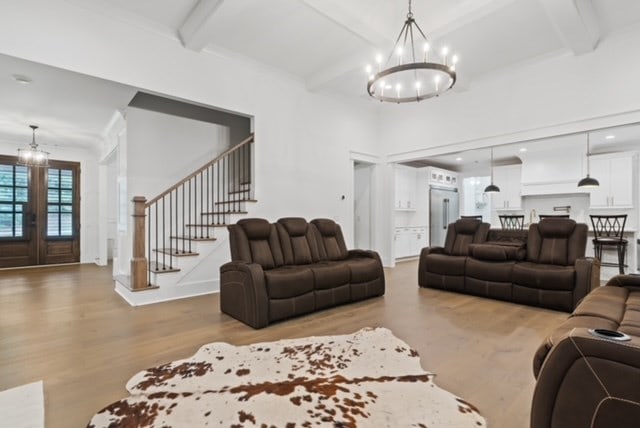 living room with beam ceiling, an inviting chandelier, light hardwood / wood-style flooring, and crown molding