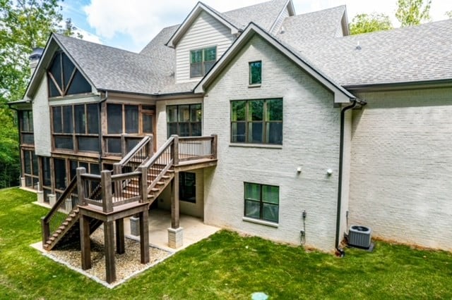 rear view of house with a lawn, a sunroom, a deck, central AC unit, and a patio