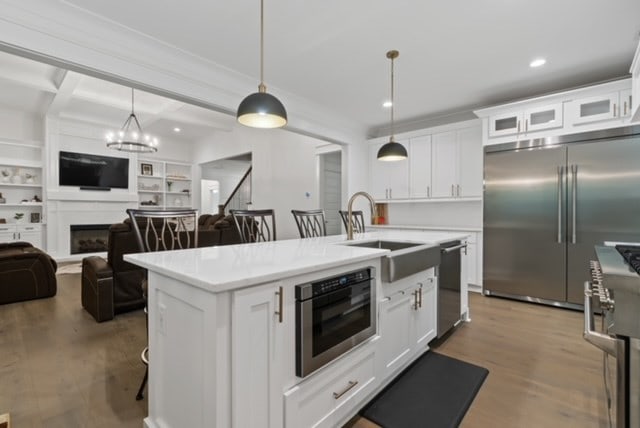 kitchen featuring sink, a center island with sink, high quality appliances, white cabinets, and hanging light fixtures