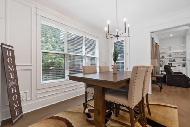 dining room featuring wood-type flooring, built in features, ornamental molding, and a notable chandelier