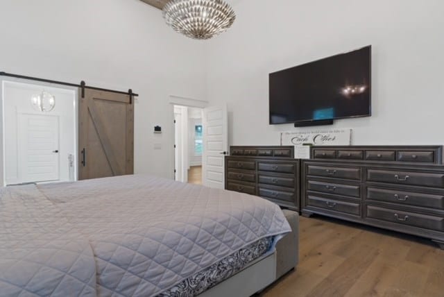 bedroom featuring a barn door, wood-type flooring, and a chandelier