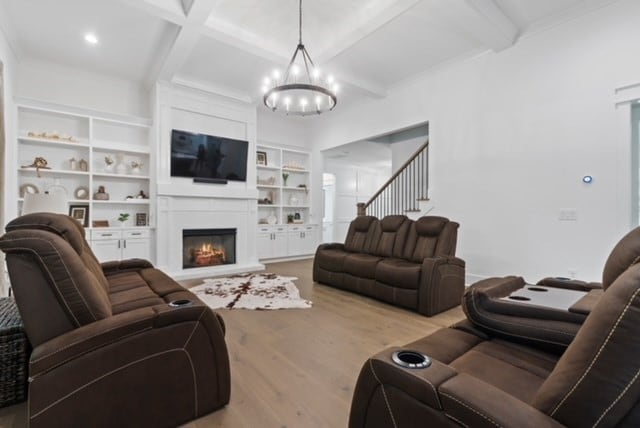 living room with built in shelves, light hardwood / wood-style floors, beamed ceiling, a large fireplace, and a chandelier