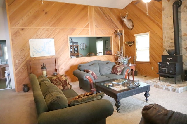 carpeted living area featuring wooden walls, vaulted ceiling with beams, and a wood stove