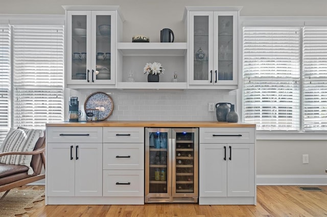 bar featuring baseboards, a bar, wine cooler, light wood-type flooring, and backsplash
