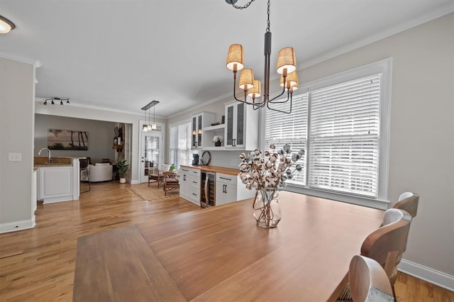 dining room with crown molding, light wood-type flooring, an inviting chandelier, baseboards, and wine cooler