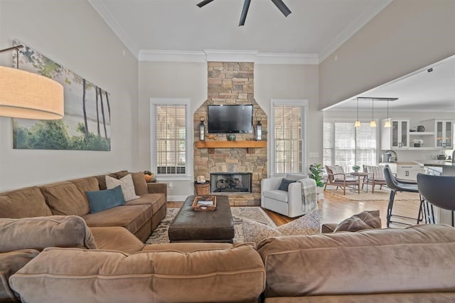 living room featuring light wood-type flooring, ornamental molding, baseboards, a ceiling fan, and a fireplace