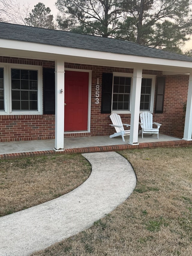 view of exterior entry with a porch and a lawn