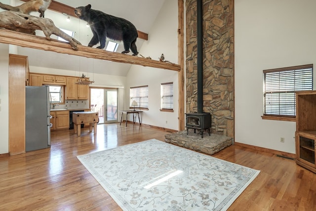 living room with a wood stove, light wood-type flooring, and high vaulted ceiling