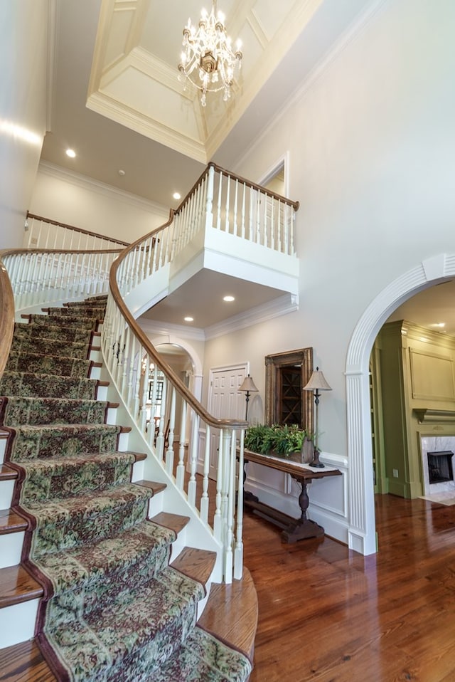 stairs featuring a high end fireplace, hardwood / wood-style floors, a towering ceiling, and crown molding