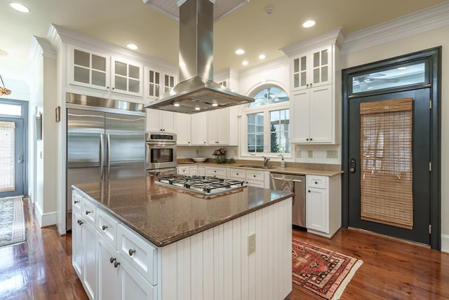 kitchen with island exhaust hood, appliances with stainless steel finishes, dark stone countertops, a center island, and white cabinetry