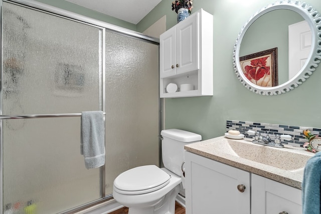 bathroom featuring vanity, toilet, a shower with door, and tasteful backsplash