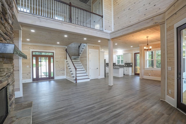 entryway featuring dark wood-type flooring, a high ceiling, an inviting chandelier, a stone fireplace, and wooden walls