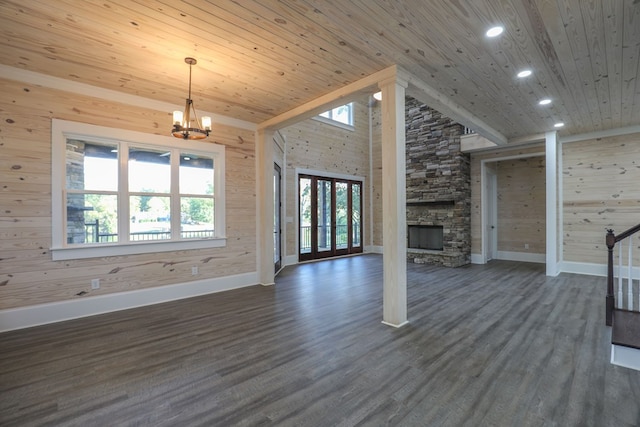 unfurnished living room featuring dark hardwood / wood-style flooring, a stone fireplace, wooden ceiling, and a notable chandelier