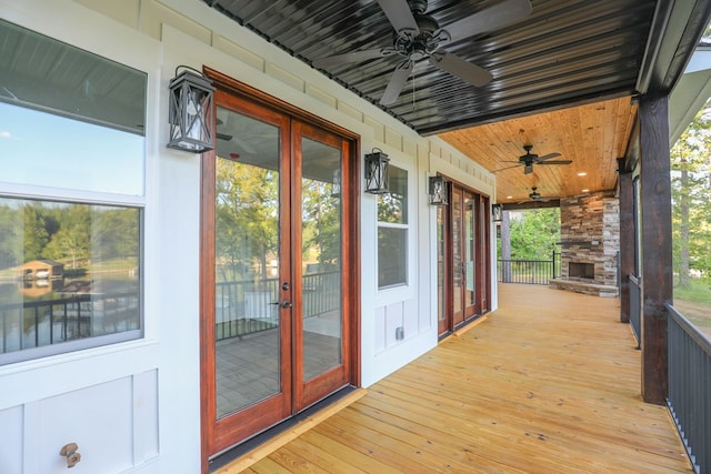 wooden terrace with french doors, a stone fireplace, and a ceiling fan