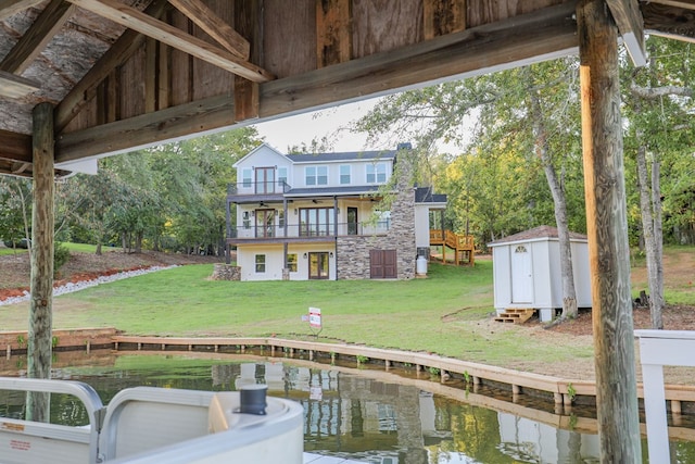 rear view of property featuring a lawn, a balcony, an outbuilding, a water view, and a shed