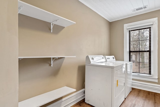 clothes washing area with hardwood / wood-style flooring, washing machine and clothes dryer, and ornamental molding