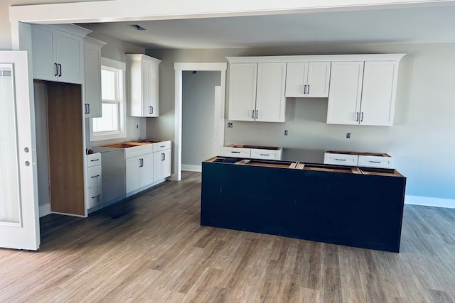 kitchen featuring white cabinetry, a kitchen island, baseboards, and wood finished floors