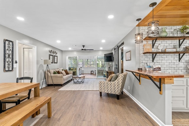 living room with ceiling fan, a barn door, and wood-type flooring