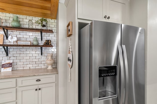 kitchen with tasteful backsplash, white cabinets, light stone countertops, and stainless steel fridge with ice dispenser